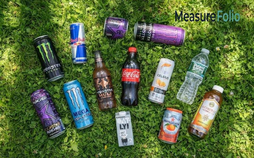 A flat-lay photograph from above shows a collection of different beverages
spread out on green grass, including energy drinks, soda, water, and juice.