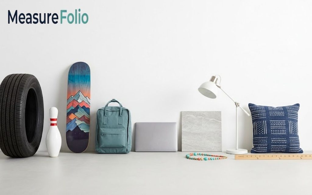 A clean arrangement of various objects, including a tire, skateboard, backpack, laptop, lamp, and pillow against a white wall.